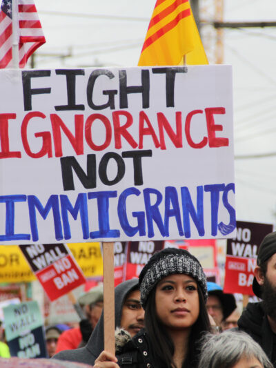 person holding protest sign saying "fight ignorance not immigrants"