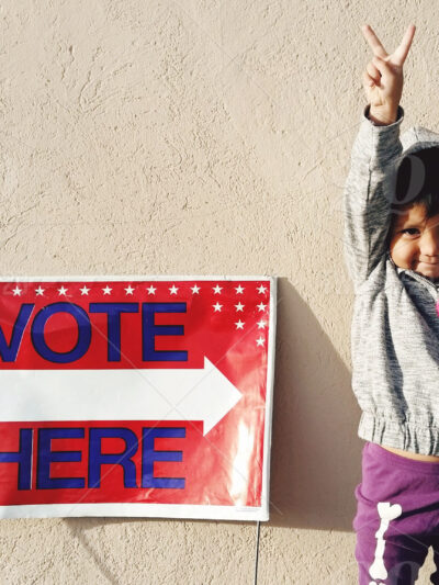 child next to a vote here sign