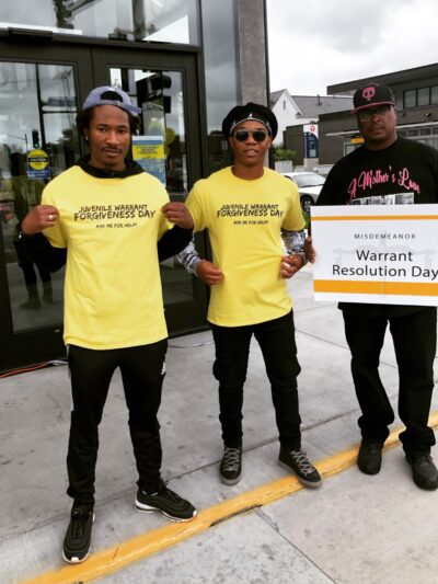 A team of volunteers outside the event displays their yellow event t-shirts which read: "Juvenile Warrant Forgiveness Day: Ask me for help"