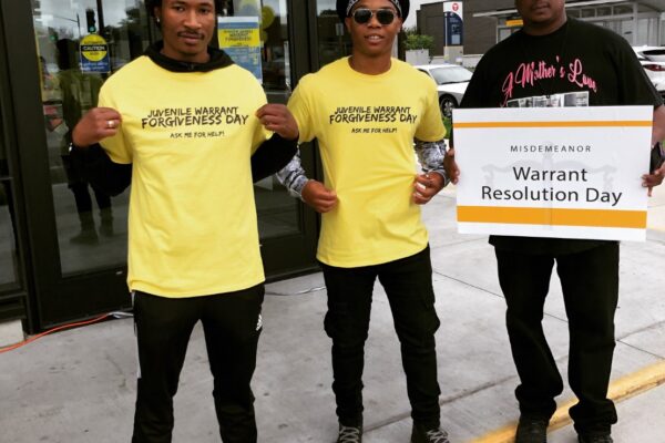 A team of volunteers outside the event displays their yellow event t-shirts which read: "Juvenile Warrant Forgiveness Day: Ask me for help"