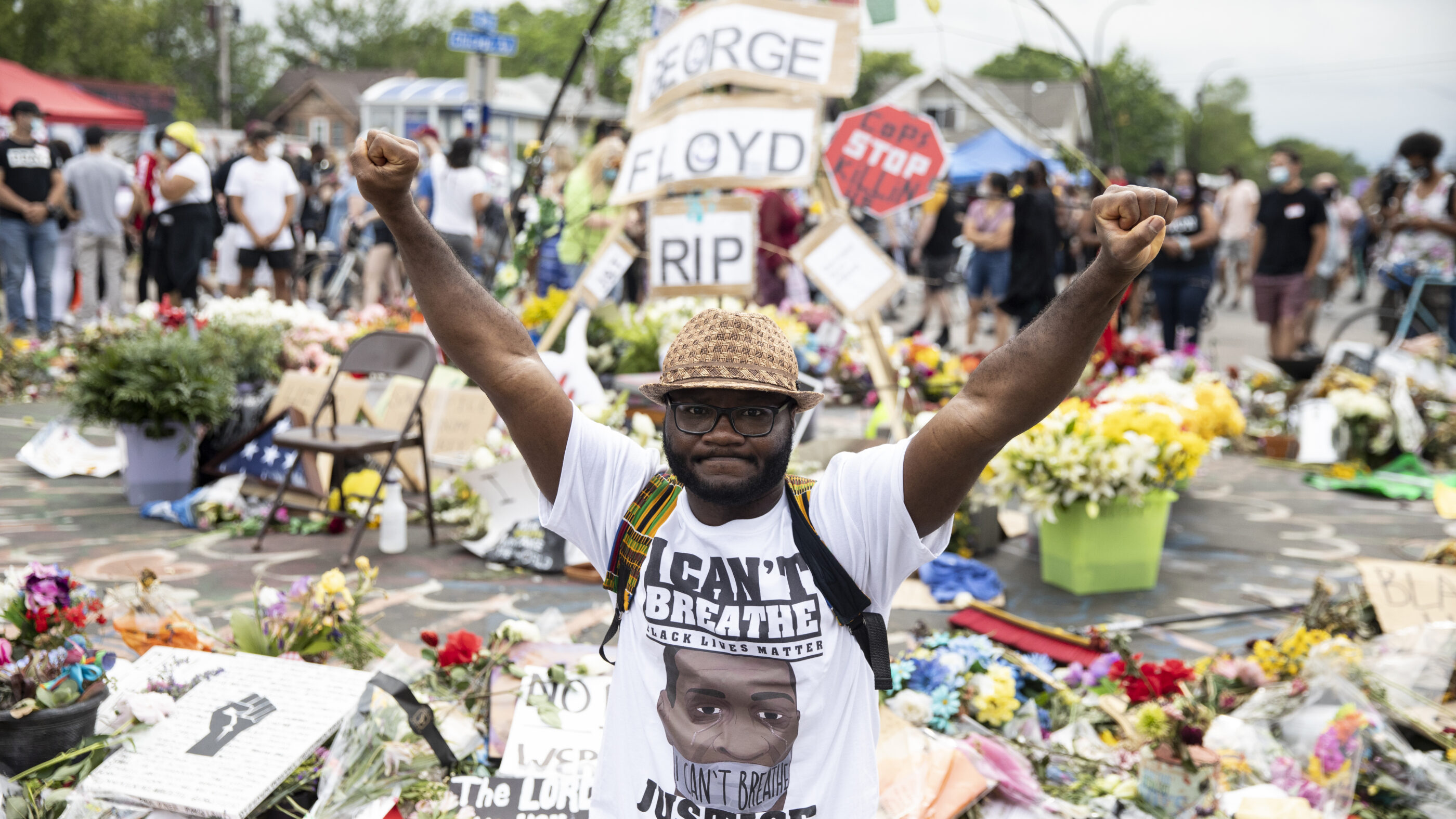 Man wearing "I Can't Breathe" tshirt stands in front of George Floyd memorial with fists raised.