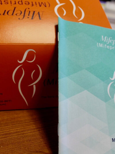An orange Mifepristone box and blue medication guide.
