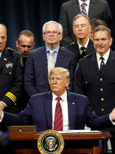 President Trump sits at podium ready to sign executive order creating a commission to study law enforcement and justice, surrounded by officers beside him in support.
