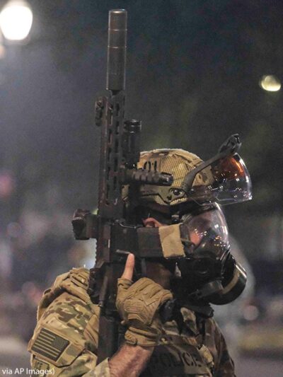 An ICE agent holds his weapon in the air as federal officers clear Main Street in Portland, Ore., on July 26, 2020.