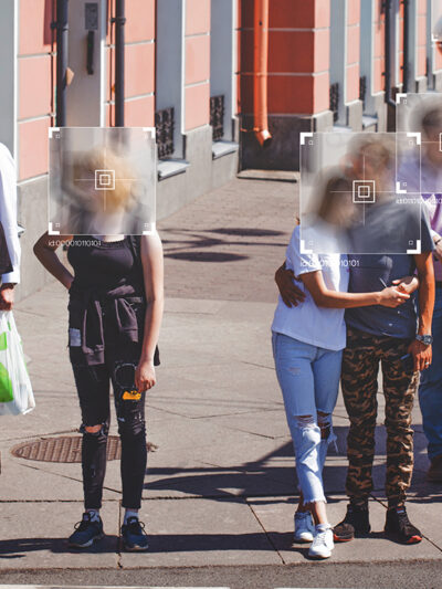 People standing at a crosswalk with face recognition software boxes superimposed over their faces.