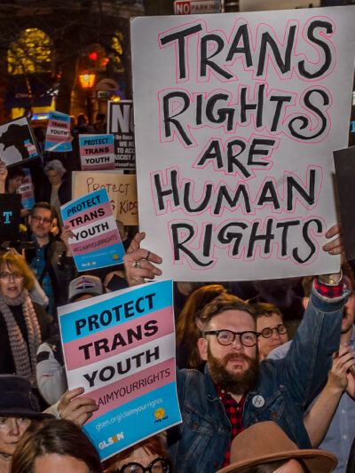 Protestors with signs advocating for the rights of trans youth.