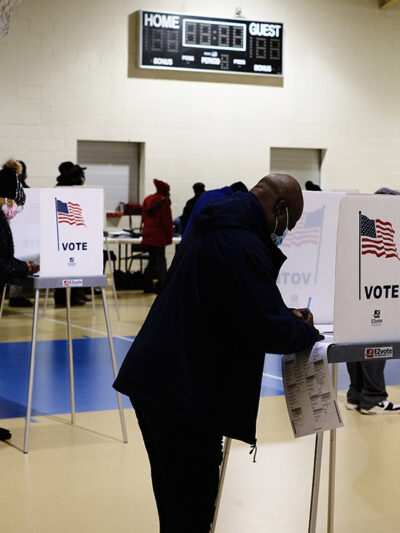 A black man filling out ballot in voting booth on Election Day.