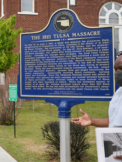 Two people explaining a sign that reads "the 1921 Tulsa Massacre" commemorating the original Black Wall Street