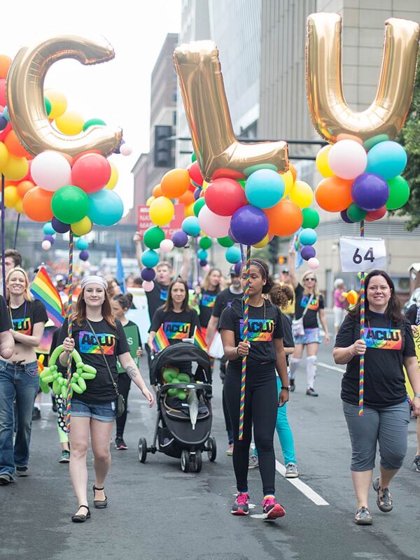 Image of people marching in the Pride parade holding up multicolored balloons reading "ACLU"