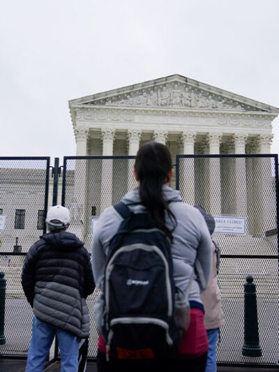 Standing beyond security gates that have signs reading "Area Closed", several people stare at the Supreme Court building.
