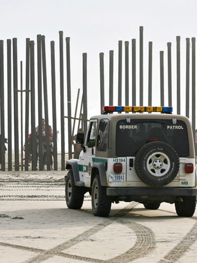 A U.S. Border Patrol vehicle sits parked in front of a crowd of people peering through the U.S.-Mexico border fence in San Diego.