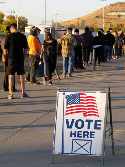 A sign that says "vote here" among a line of voters.
