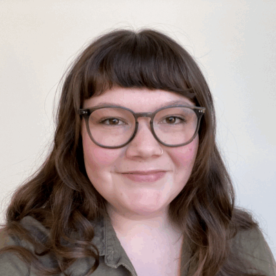 Rachel Fergus is ACLU-MN's communications associate. In her portrait, she is wearing an olive green collared top and has plastic framed glasses on. She is brunette with wavy hair and bangs.