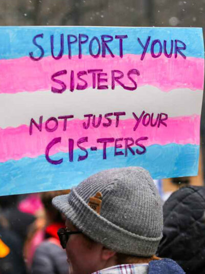 A demonstration sign reading "Support Your Sisters, Not Just Your Cis-ters."