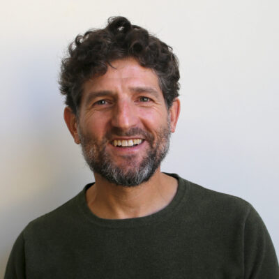 Photo of Ben wearing a dark green sweater standing against a white wall.
