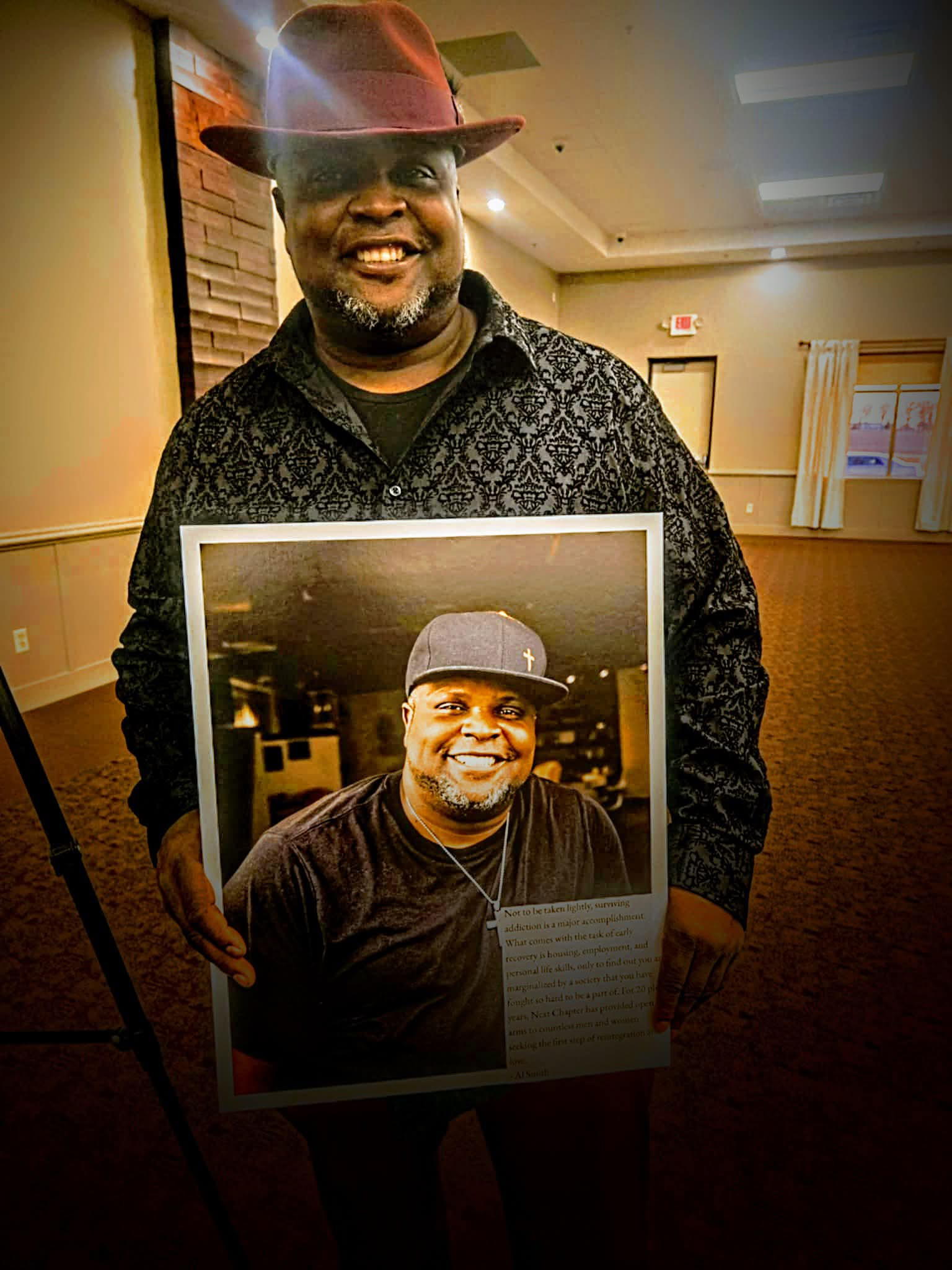 Photo of Al wearing a red hat and a long sleave shirt holding a photo of himself.