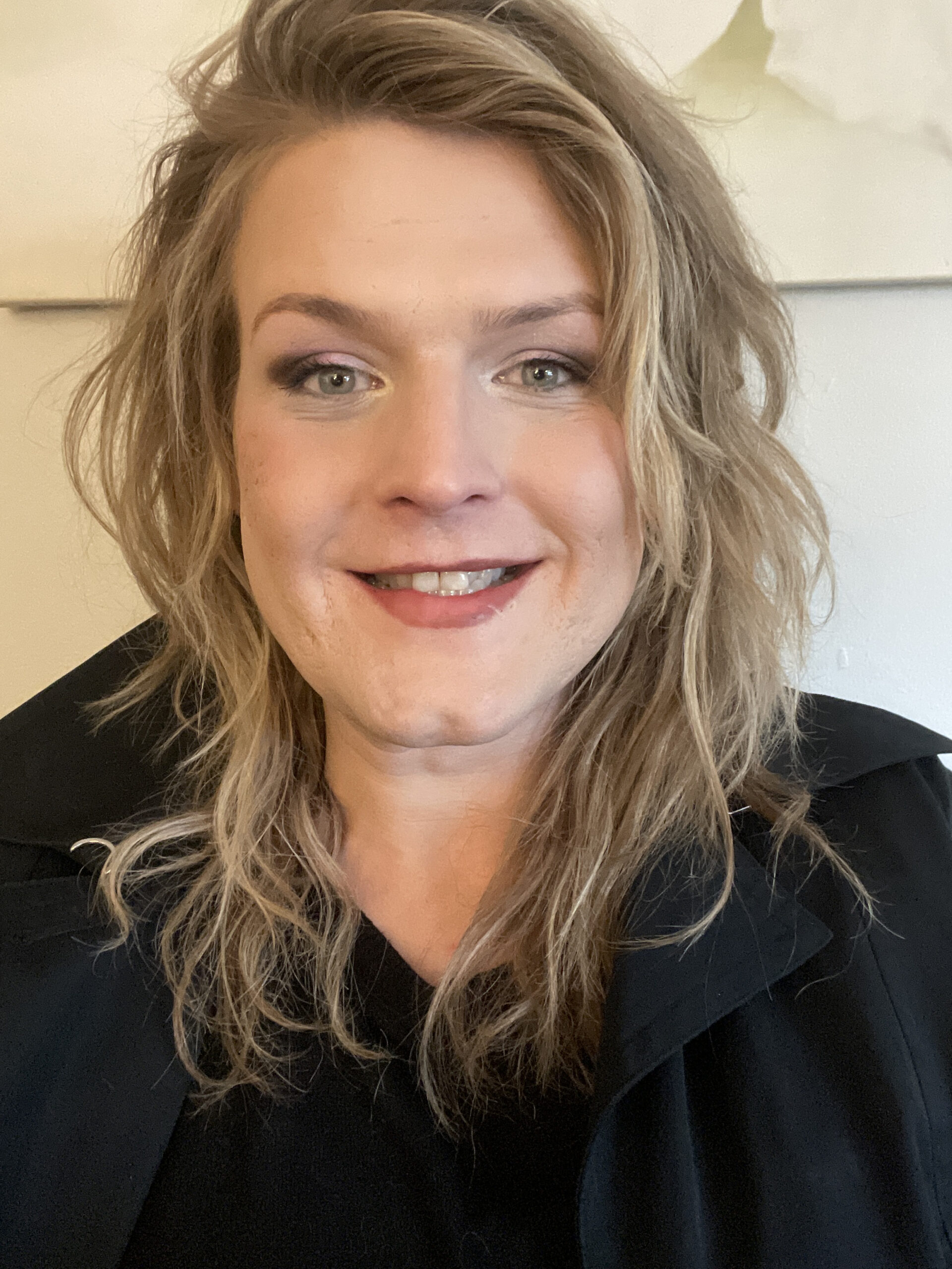 Headshot of Alessandra with medium length blonde hair and a black, collard shirt