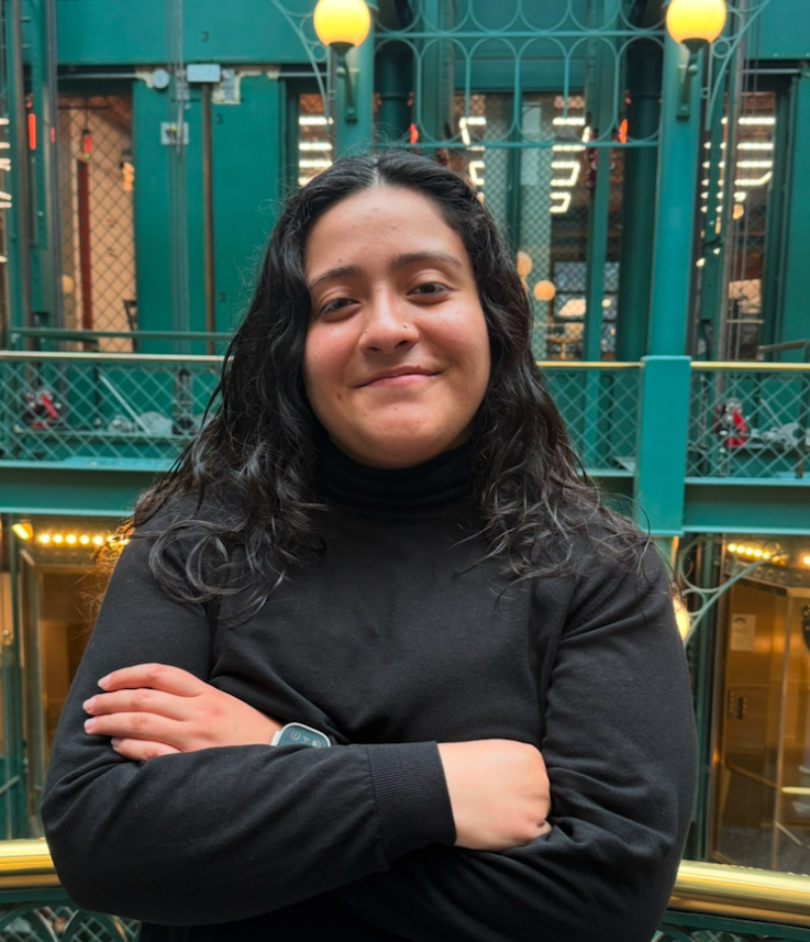Photo of Myrka wearing a black turtleneck with an old blue and yellow building interior behind her.