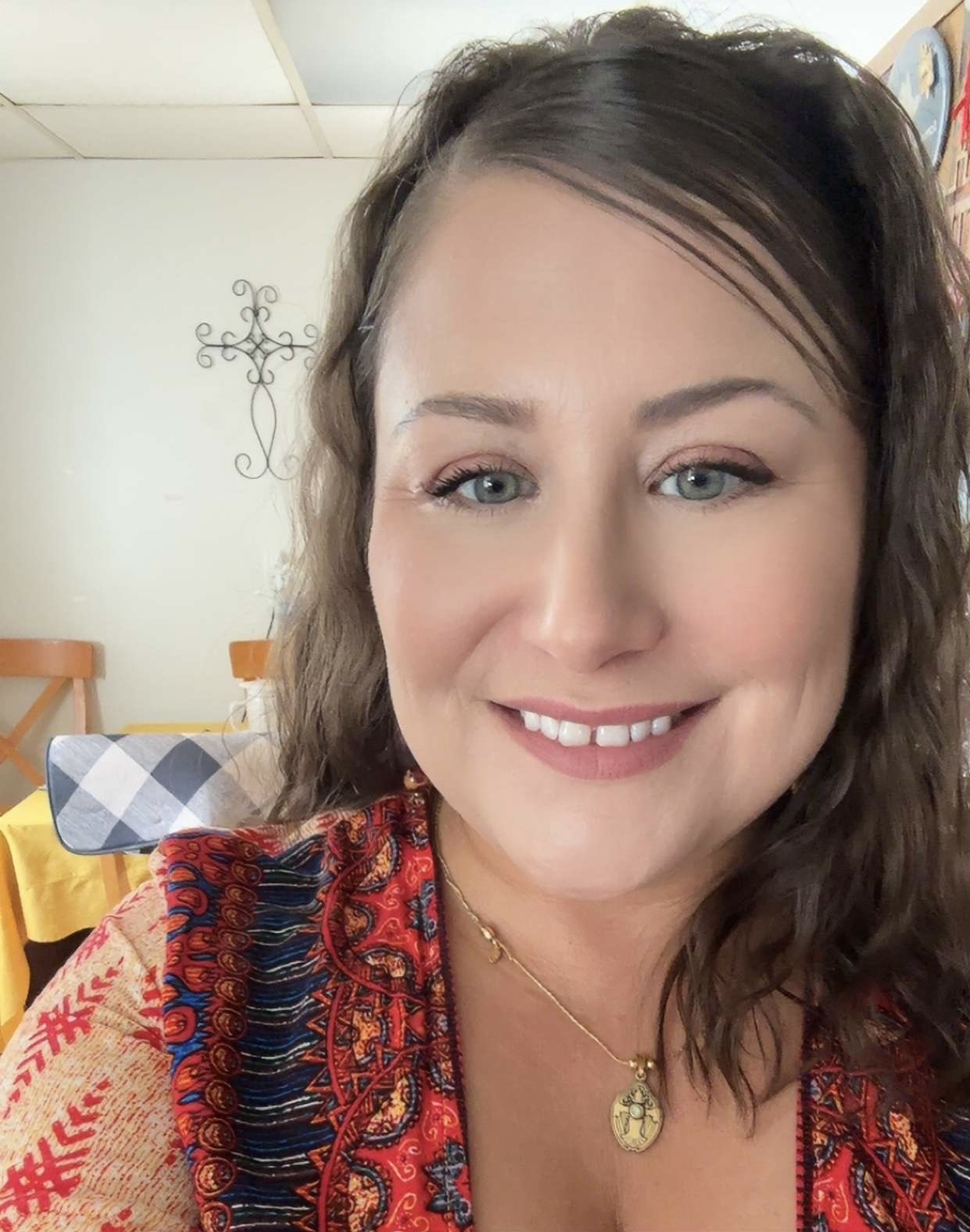 Headshot of Natasha with medium brown hair and a red, blue and cream blouse with multiple patterns.