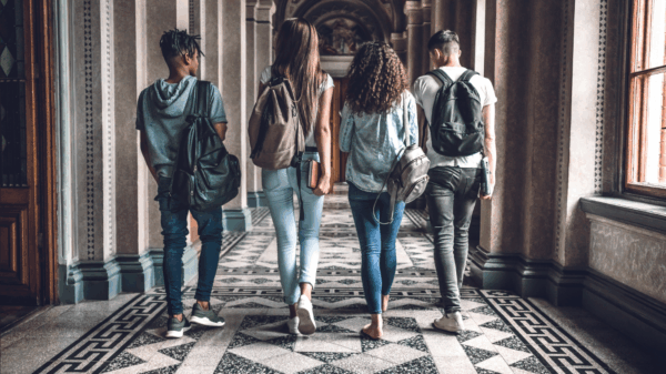 Photo of four college students wearing backpacks walking down a hallway with marble floor.