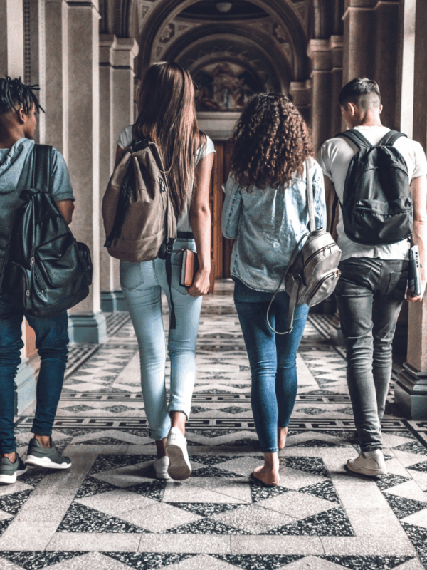 Photo of four college students wearing backpacks walking down a hallway with marble floor.