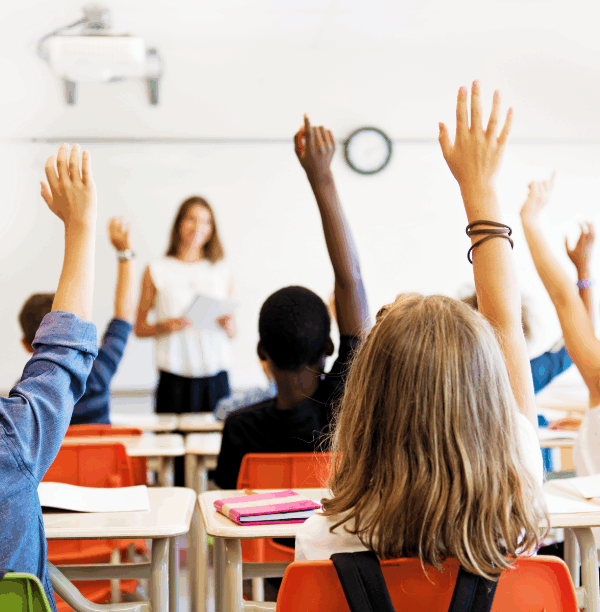 Photo of a classroom with students raising their hands and facing the teacher