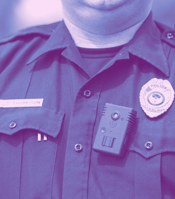 Blue photo of police officer's chest. He is wearing his badge and a body worn camera.