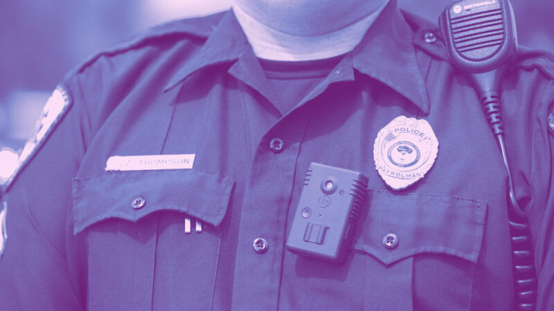 Blue photo of police officer's chest. He is wearing his badge and a body worn camera.