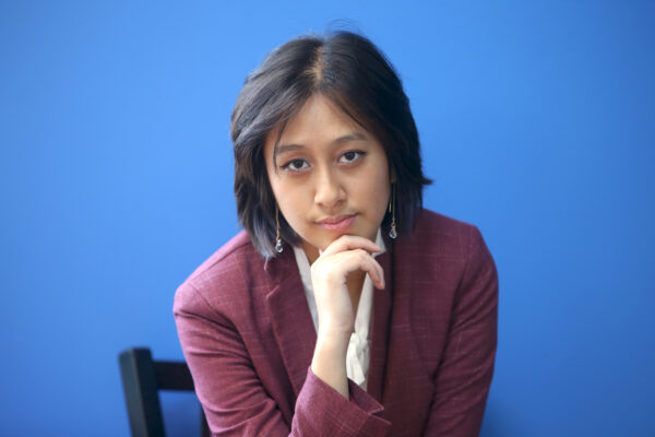 Photo of Willow looking into the camera wearing a maroon blazer in front of a blue wall.