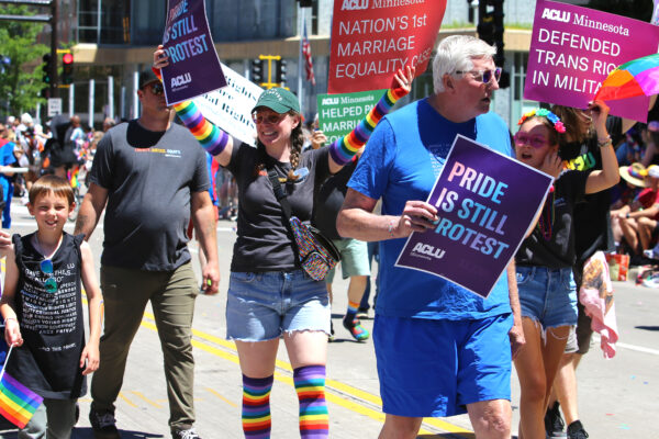 Photo of people marching in a parade. One person has a sign that says, "ACLU Minnesota defends equal education for trans teens."