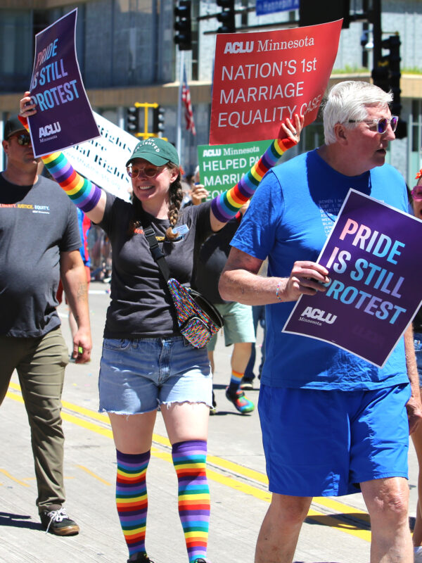 Photo of people marching in a parade. One person has a sign that says, "ACLU Minnesota defends equal education for trans teens."