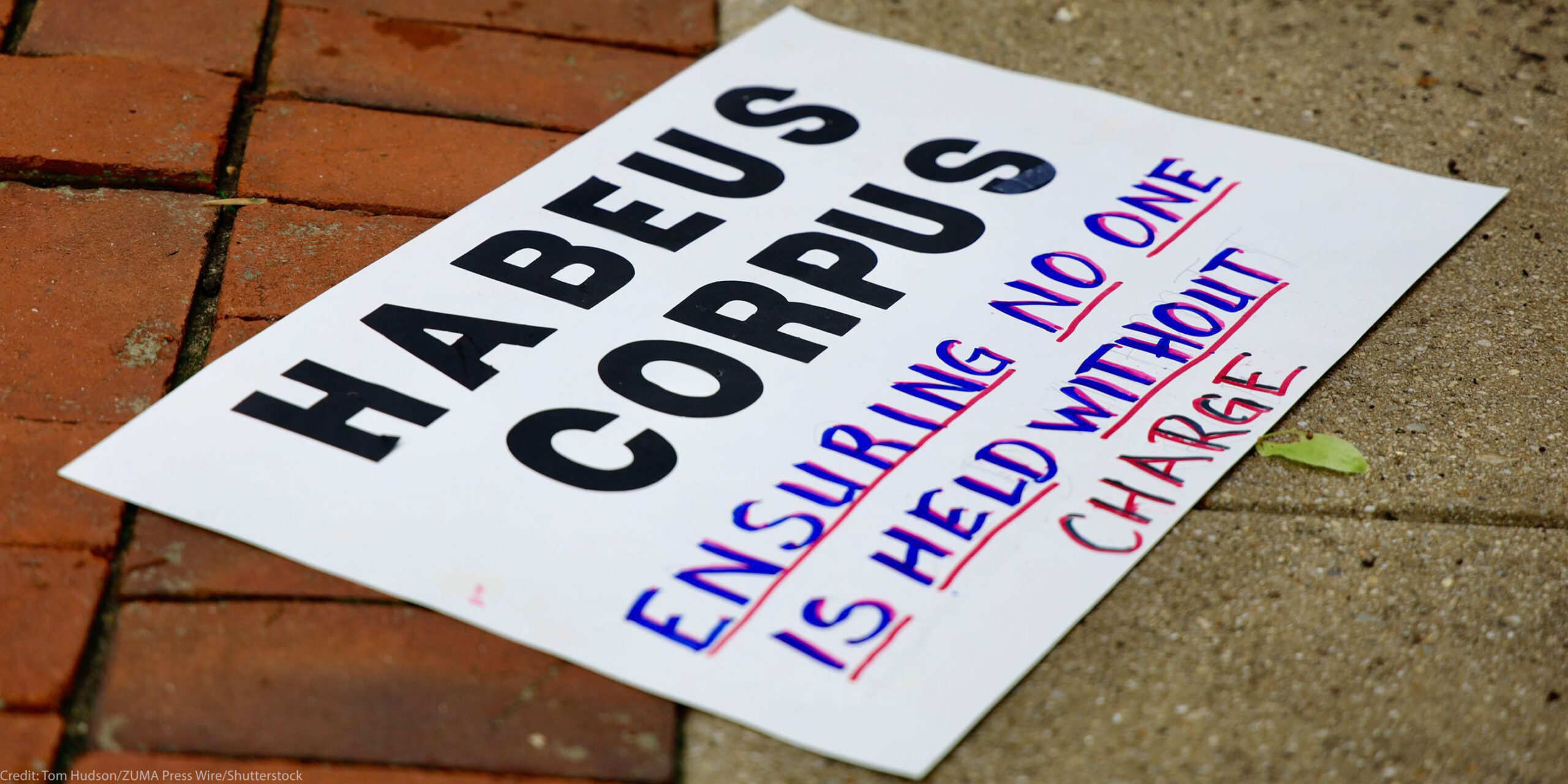 A sign reading " HABEAS CORPUS Ensuring No One is Held Without Charge" lying on the ground.