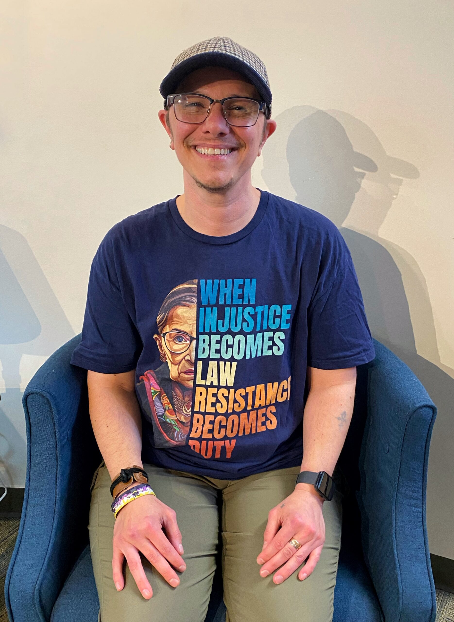 Photo of Ray wearing a blue t-shirt with a Ruther Bader Ginsburg quote, tan pants and a plaid ballcap.