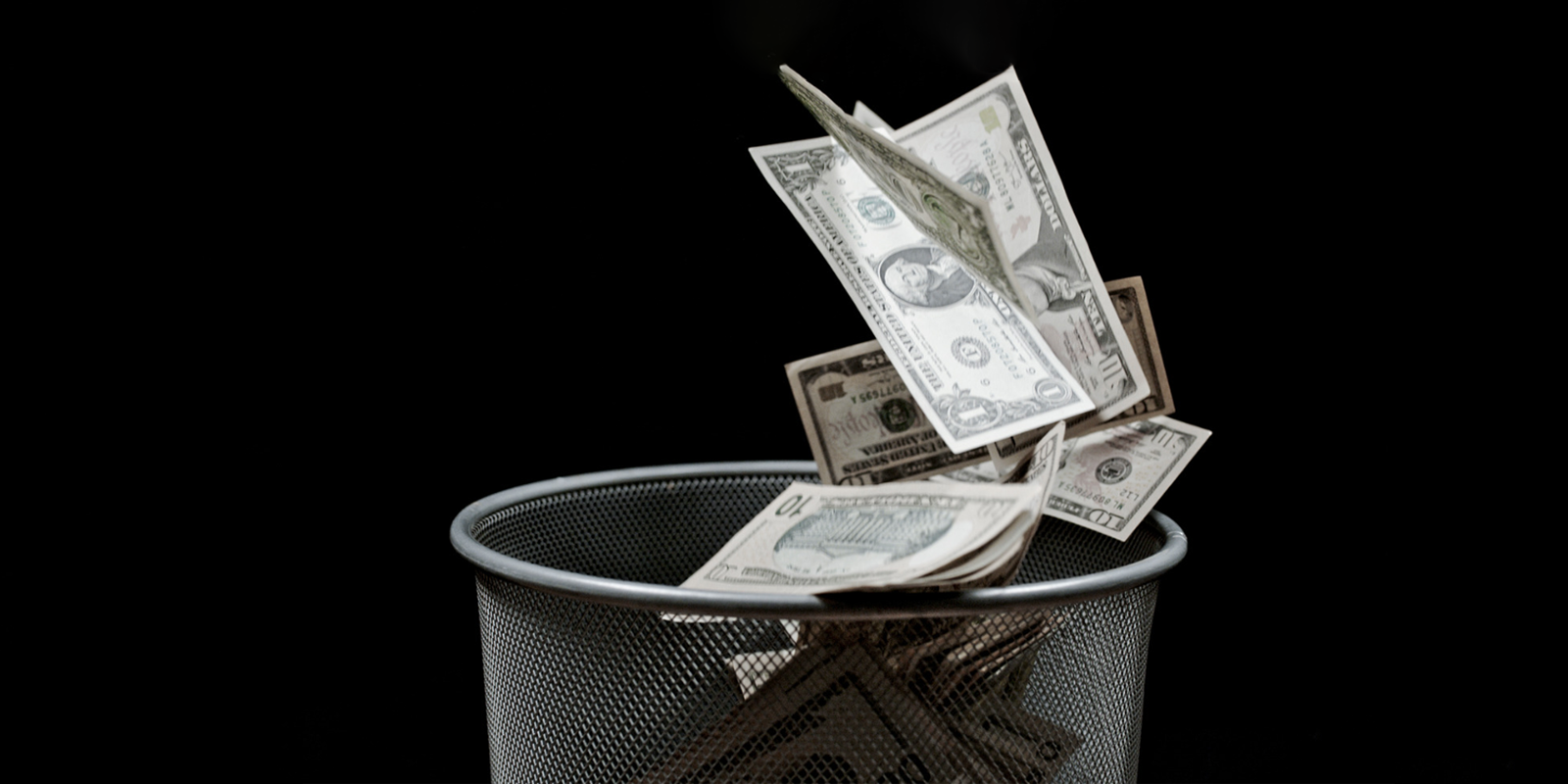 Money falling into a silver waste basket