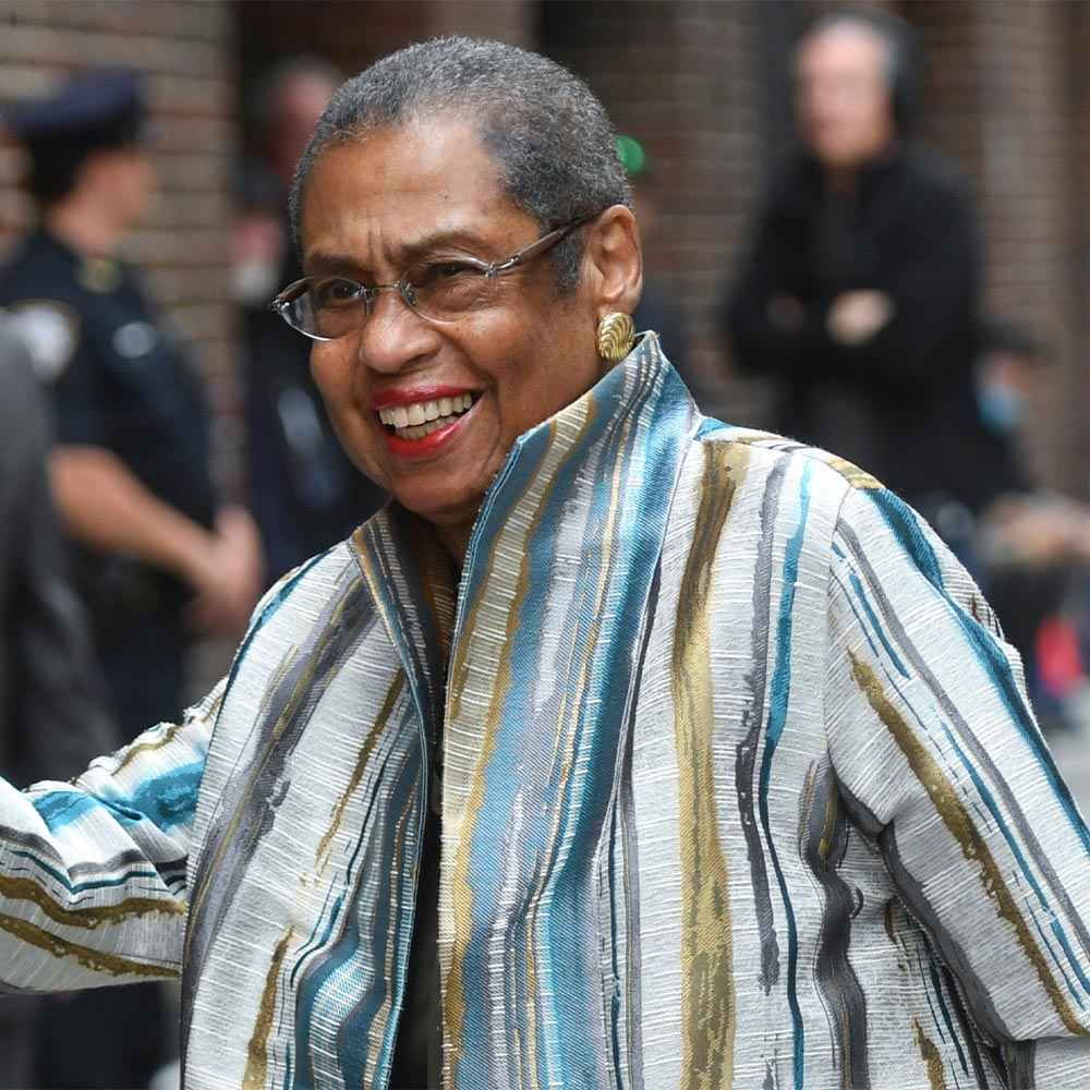 Congresswoman Eleanor Holmes candidly smiles. She is wearing a gray jacket with gold and blue vertical stripes. 