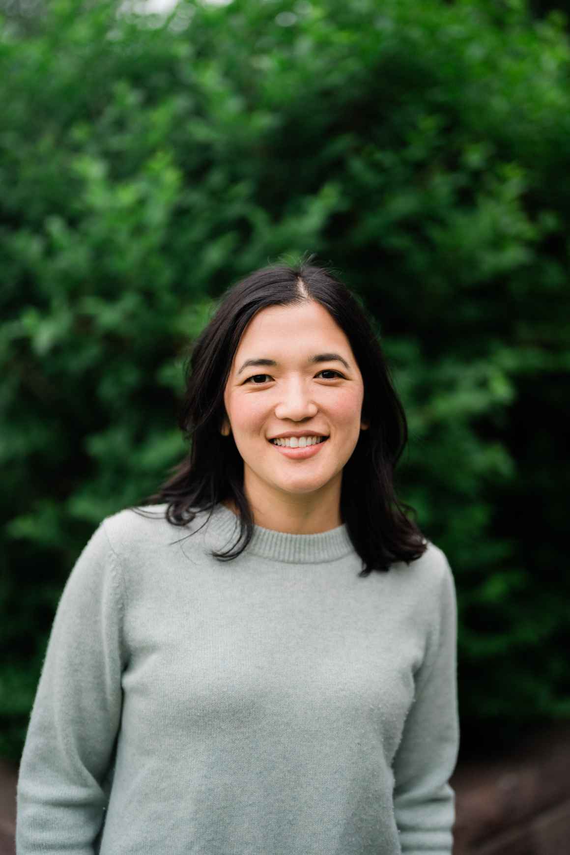 Board candidate Jenny Lee smiles in front of a green back drop.