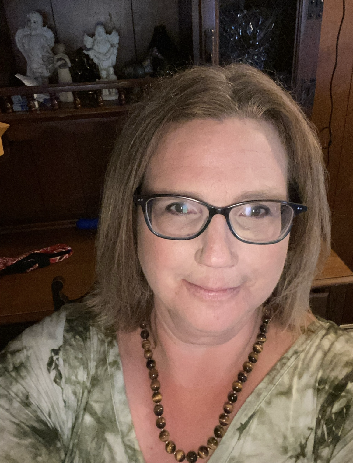 Headshot of Machelle wearing glasses with dark rims, a green top and a necklace made with brown beads.