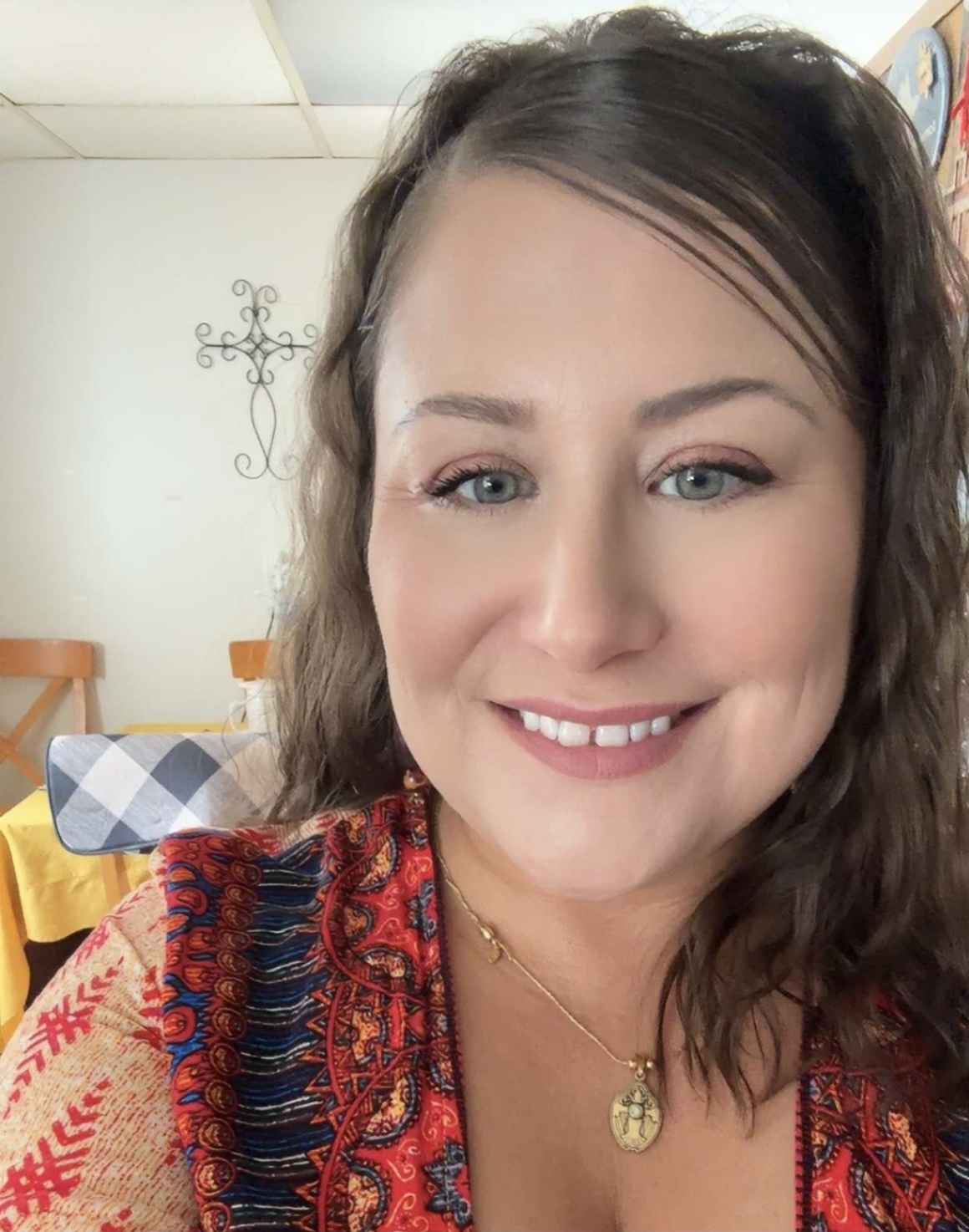 Headshot of Natasha with medium brown hair and a red, blue and cream blouse with multiple patterns.