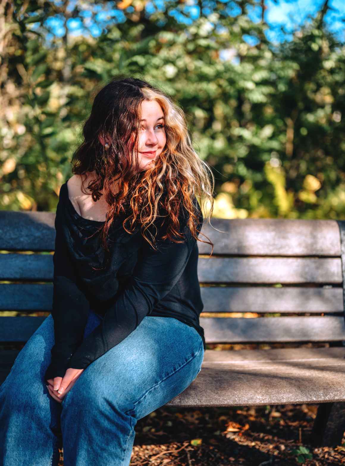 Photo of Rowan by JoJo's Photos & Studio Photo of Rowan sitting on a bench outside wearing a black long sleeve shirt and blue jeans.