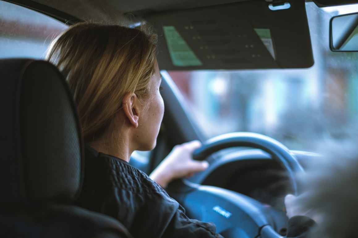 Photo from back passenger seat in car of a woman driving. 