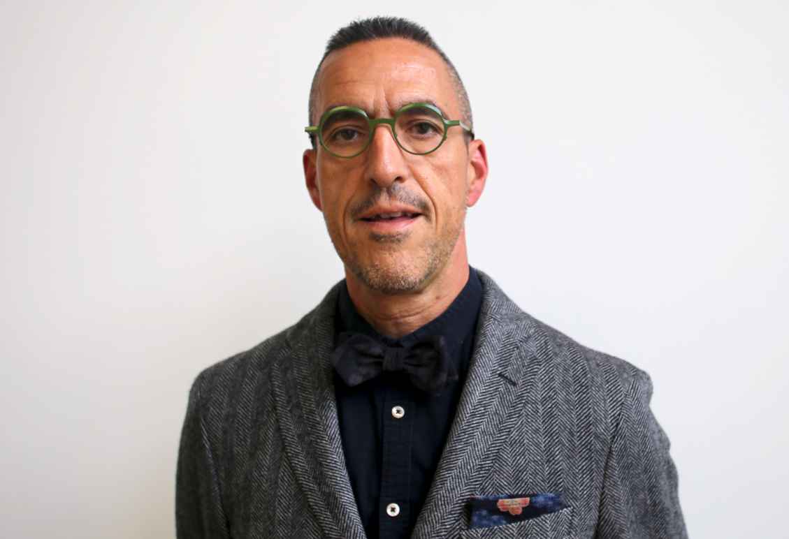 Jim Rowader wearing a grey suit jacket, dark button-down shirt and green circular glasses