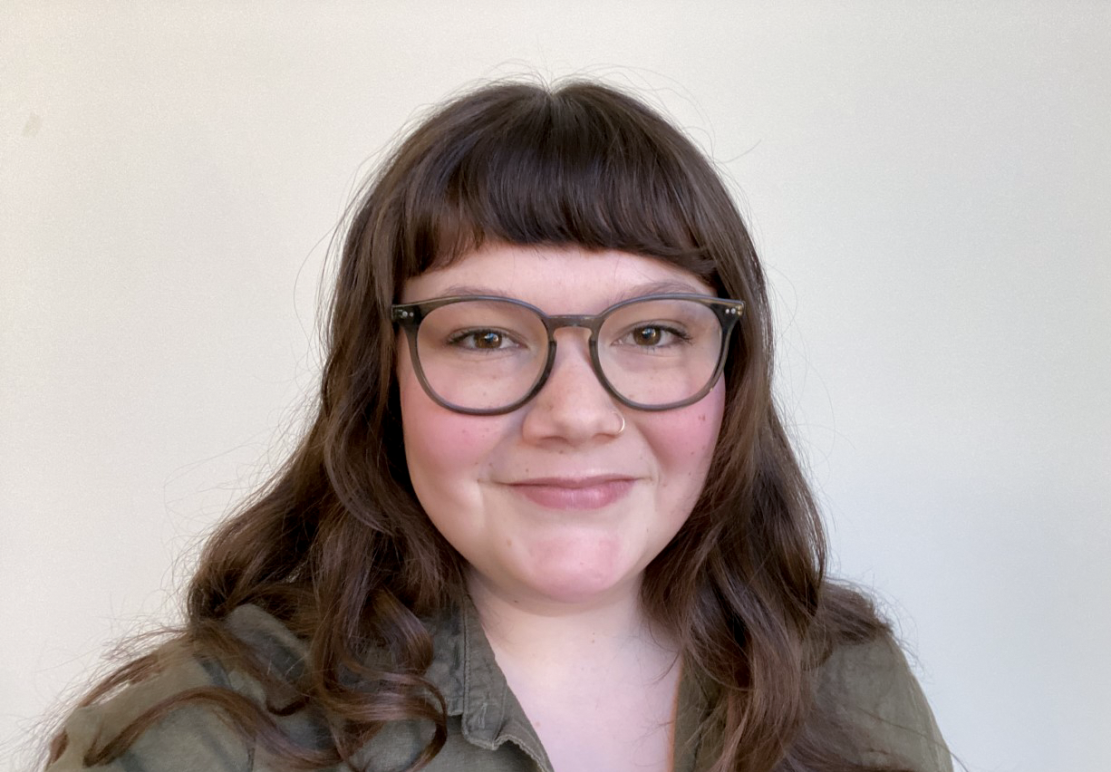 Rachel Fergus is ACLU-MN's communications associate. In her portrait, she is wearing an olive green collared top and has plastic framed glasses on. She is brunette with wavy hair and bangs.
