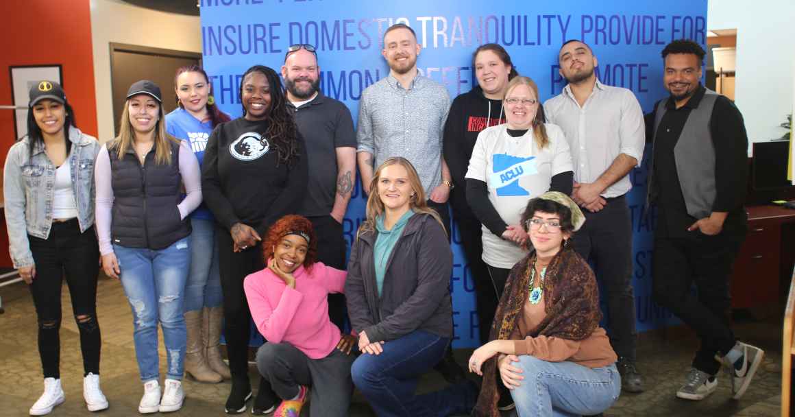 Photo of 10 Smart Justice Fellows, ACLU-MN Organizer Paul Sullivan, and two T.O.N.E. U.P. staff members standing and kneeling in a group and smiling at the camera. 