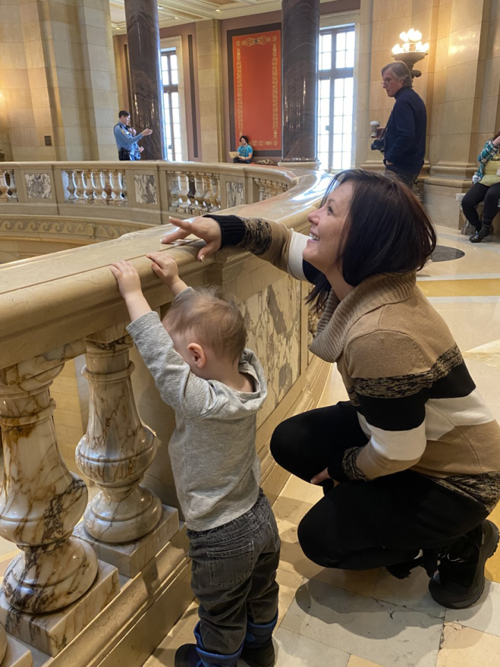 ACLU-MN client Jennifer Schroeder leans against the Capitol rotunda railing with her 2-year-old son.
