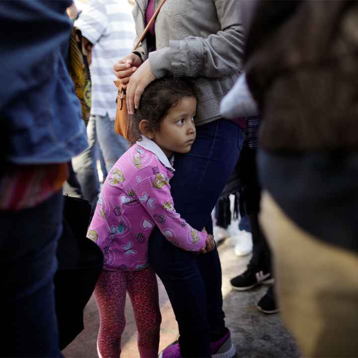 A young child holds on to her mother legs as they wait with other families to request political asylum in the United States, across the border in Tijuana, Mexico.