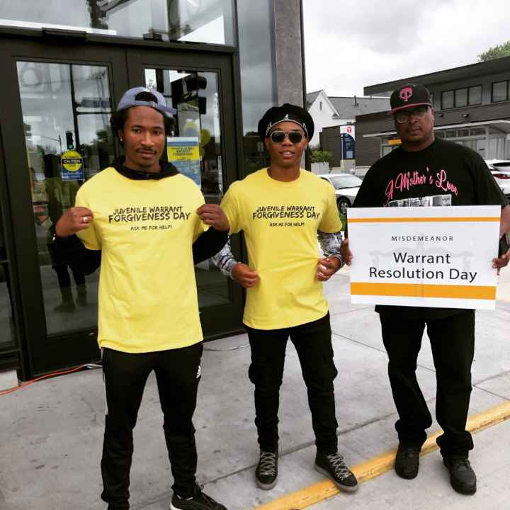 Juvenile Warrant Forgiveness Day Volunteers A team of volunteers outside the event displays their yellow event t-shirts which read: "Juvenile Warrant Forgiveness Day: Ask me for help"