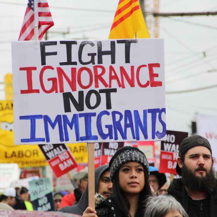 person holding protest sign saying "fight ignorance not immigrants" 