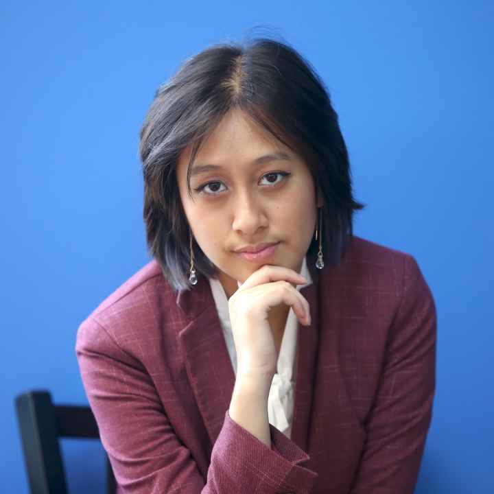 Photo of Willow looking into the camera wearing a maroon blazer in front of a blue wall.