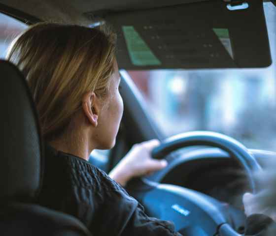 Photo from back passenger seat in car of a woman driving. 